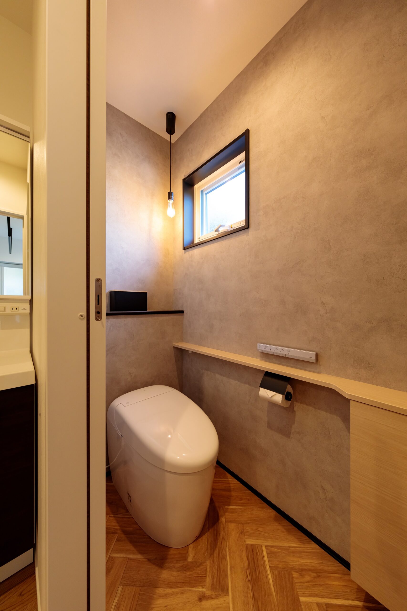 モルタル調のアクセントクロス×ヘリンボーンフロアの組合せがお洒落。トイレ内に手洗い器を設置しないスタイルも、「掃除の手間を減らせるように」と考えられたK様のこだわりです。