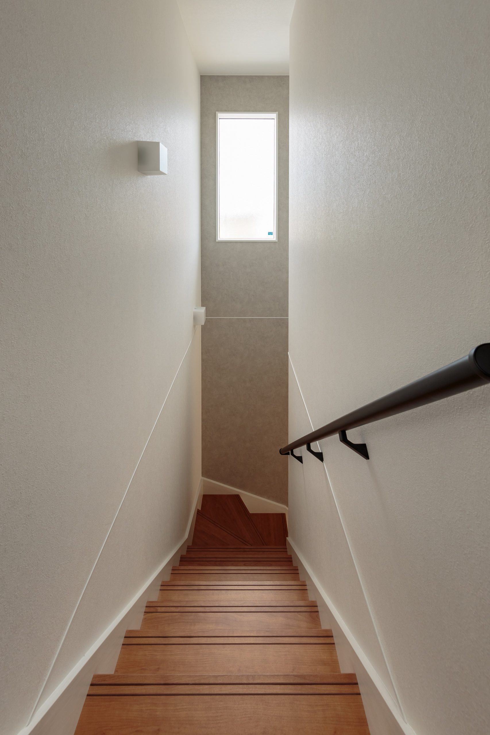 グレーのクロスとブラックの手摺りを差し色にした階段スペース。天井が高く、階段を行き来するたびに開放的な気分になれるそう。高い位置から光が差し込み、階下のリビングに明るさを届けてくれます。
